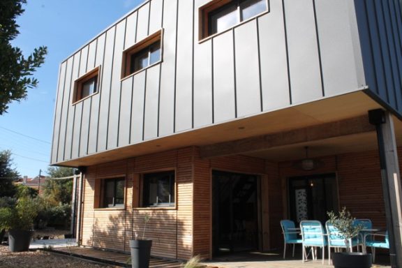 Bardage en joint debout Maison moderne avec façades en métal et en bois, fenêtres et terrasse avec chaises.